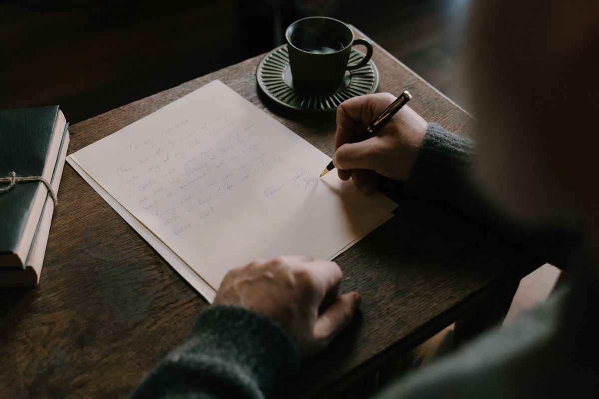 A person composing a handwritten letter at a desk