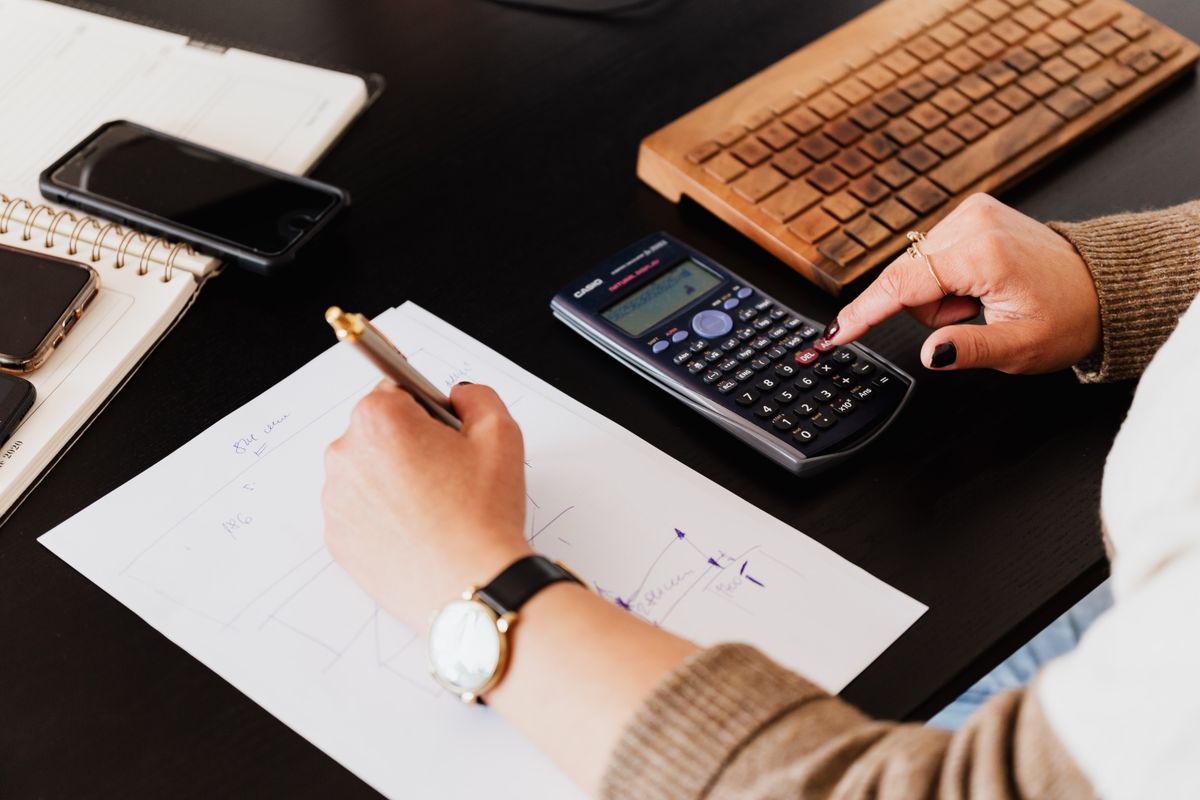 A bookkeeper using a calculator and recording figures in a notebook