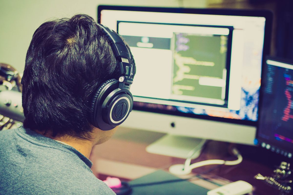 A programmer wearing headphones and working at two computer monitors
