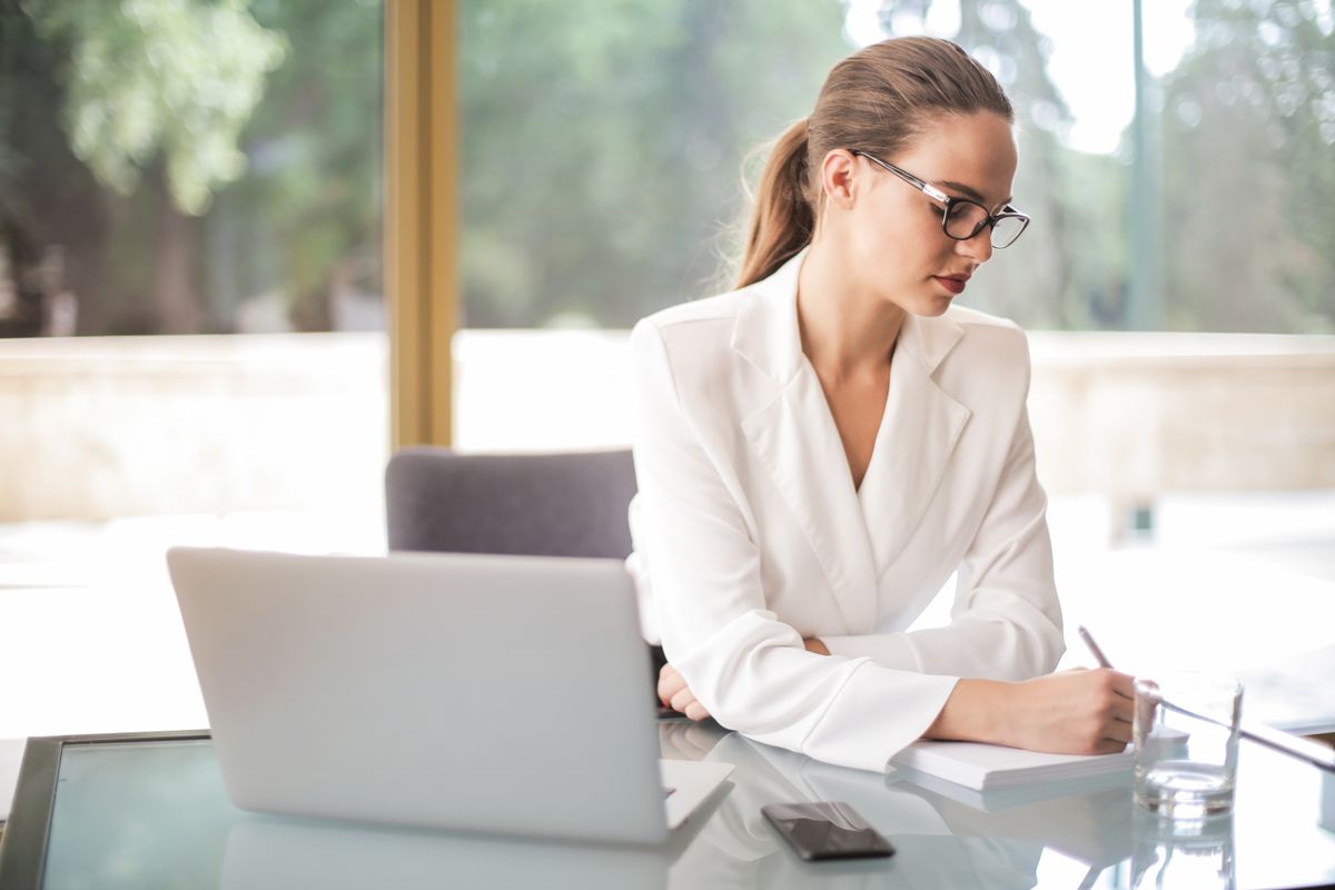 A professional taking notes beside a laptop in a bright office