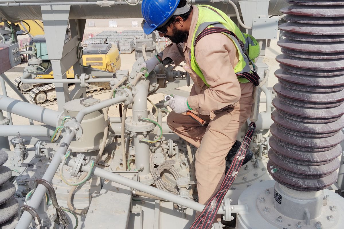 A worker in a safety helmet and reflective vest inspecting industrial pipes